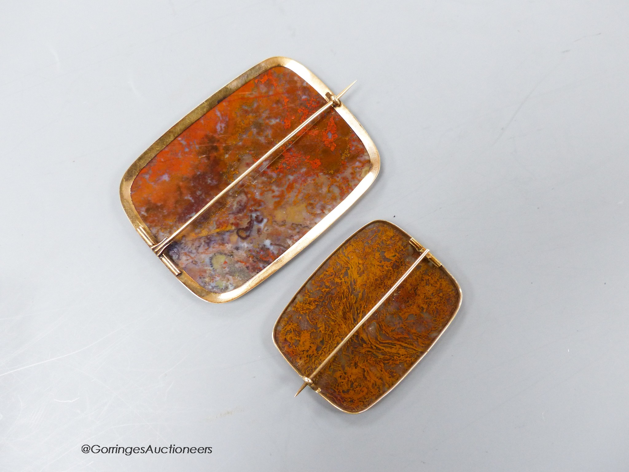 Two early 20th century yellow metal mounted agate shaped square brooches, largest 74mm, gross weight 42 grams.